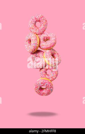 Amazing donuts on soft pink background. Top view of yummy fresh homemade doughnuts. Decorated with confetti in shape of little hearts. Levitation.  Stock Photo