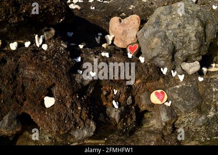 Heart shaped coral and stones, painted with bright red "love" hearts, placed in volcanic rocks on shoreline at Sandy Beach Park, Oahu, Hawaii, USA Stock Photo