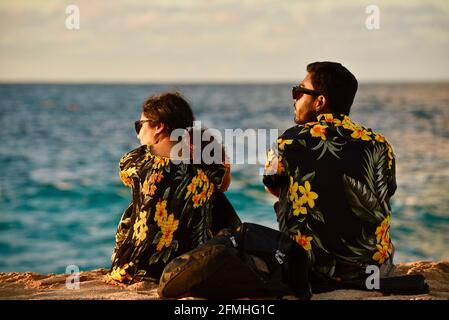 Married couple watching sunset, wearing matching Hawaiian shirts with flower prints, Sunset Beach, Haleiwa, Hawaii, USA Stock Photo