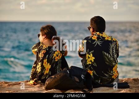 Married couple watching sunset, wearing matching Hawaiian shirts with flower prints, Sunset Beach, Haleiwa, Hawaii, USA Stock Photo