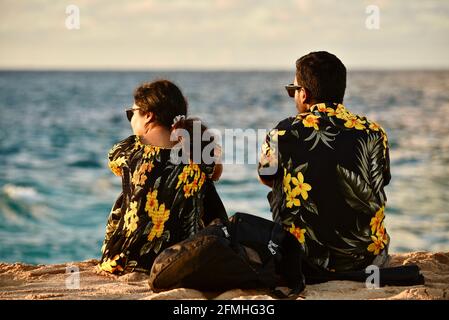 Married couple watching sunset, wearing matching Hawaiian shirts with flower prints, Sunset Beach, Haleiwa, Hawaii, USA Stock Photo