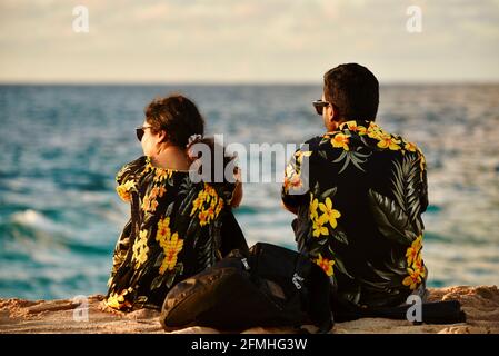 Married couple watching sunset, wearing matching Hawaiian shirts with flower prints, Sunset Beach, Haleiwa, Hawaii, USA Stock Photo