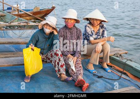 Three Vietnamese women sat on boat by the riverside in old town Hoi An, Vietnam Stock Photo