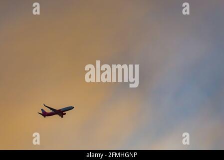 The plane comes in for a landing against the darkening sky. Blue-yellow sky and the plane in it in the lower right corner. Stock Photo