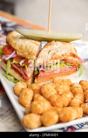 A spicy Italian sandwich with ham, salami, peppers, onions, tomatoes, pickle, cheese, and lettuce.  Served at an out door restaurant cafe. Stock Photo