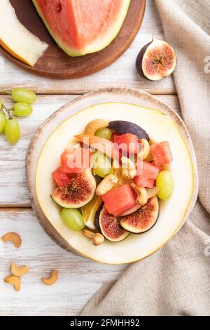 Vegetarian fruit salad of watermelon, grapes, figs, pear, orange, cashew on white wooden background and linen textile. Top view, flat lay, close up. Stock Photo