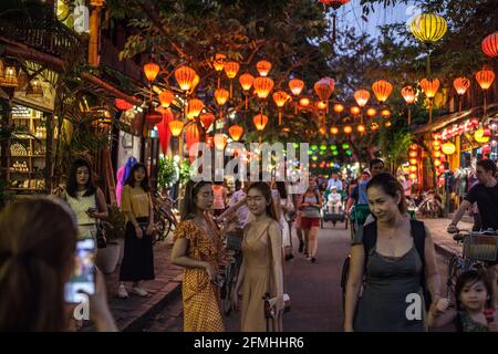 Attractive female tourists posing beneath colourful lanterns hanging between buildings in the old town, Hoi An, Vietnam Stock Photo