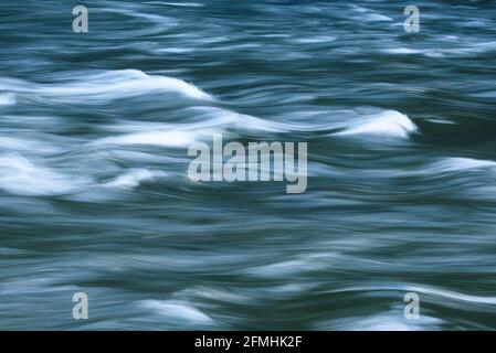 Abstract of a flowing river captured in slow motion with white caps in a  rolling motion of sweeping curves Stock Photo