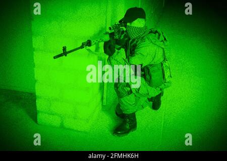 Mercenary sniper firing sniper rifle inside the building. View through night vision. Stock Photo