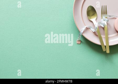 Plate and fork, spoon with measuring tape on green background. Diet concept Stock Photo