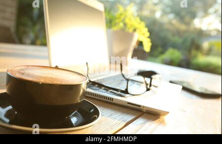 Beautiful golden morning sunshine on an outdoor table setting with hot coffee, a laptop computer, mobile phone, glasses and mouse set up for online sh Stock Photo