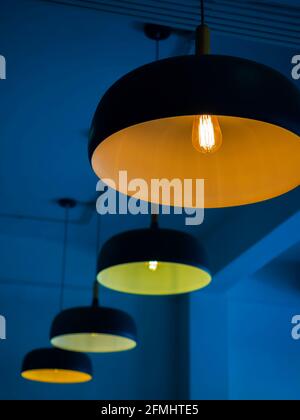 Row of modern round ceiling lights with yellow light bulbs hanging from ceiling in the dark  building construction, vertical style. Stock Photo