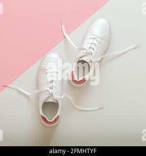 White sneakers with flying laces, female white leather shoes with laces on pink background. Pair of stylish sneakers Comfortable sportswear hipster Stock Photo