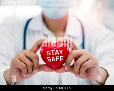 Stay Safe, healthcare and medicine concept. Close up of female doctor hands holding the red heart with word Stay Safe, Campaign for people to stay hom Stock Photo