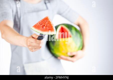 A young caucasian woman is cutting a wedge out of a ripe watermelon using a knife. Melon is ripe with field spot. Light and airy summer season fruit c Stock Photo