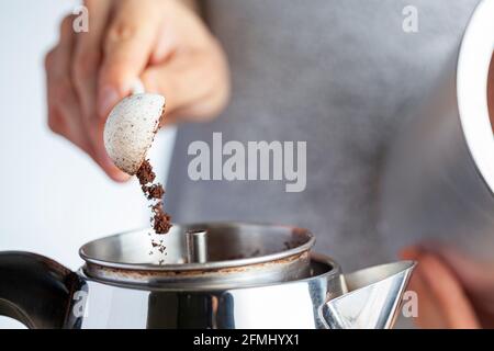 A caucasian woman is taking a teaspoon of ground coffee from a jar using a plastic measuring spoon and putting it into a percolator for brewing homema Stock Photo