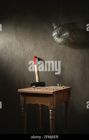 Hammer with small transparent balls on wooden vintage stool under hanging vase on rope on gray background Stock Photo