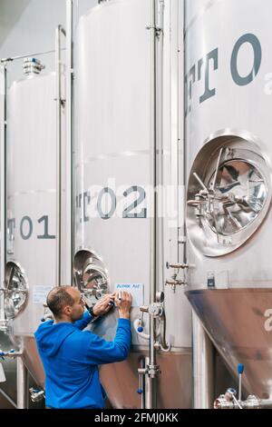 Back view of male engineer taking notes on paper on metal vessel in beer factory Stock Photo