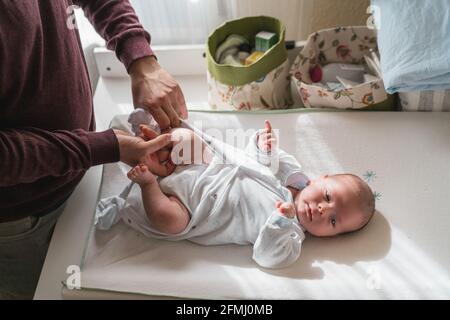 From above of crop unrecognizable father dressing charming newborn baby at home in sunlight Stock Photo