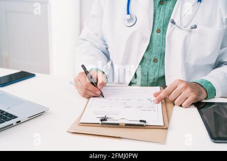 Cropped unrecognizable uniform with stethoscope taking notes on paper sheet while working in clinic Stock Photo