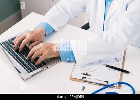 From above cropped unrecognizable male doctor in uniform typing on netbook at table with stethoscope in clinic Stock Photo