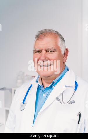 Cheerful senior male doctor in white robe with stethoscope looking at camera in hospital Stock Photo