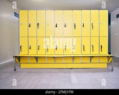 Modern bright lockers in rows with keys above bench between narrow corridors in light building Stock Photo
