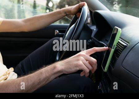 Side view of cropped unrecognizable male driver checking direction on GPS navigator on smartphone while traveling through countryside in summer day Stock Photo