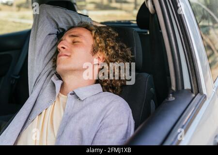 Relaxed young male traveler sleeping on driver seat of modern automobile while resting during road trip through countryside in summer day Stock Photo
