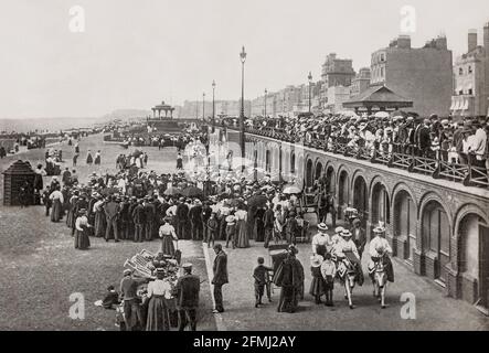 A late 19th Century view of the seafront at Brighton in East Sussex, England. King George IV spent much time in the town and constructed the Royal Pavilion there. The arrival of the London and Brighton Railway in 1841 brought Brighton within the reach of day-trippers from London. Many of the major attractions were built during the Victorian era, such as the Grand Hotel (1864), the West Pier (1866), and the Palace Pier (1899). Stock Photo