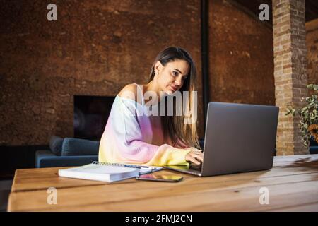 Content female remote employee with cellphone and netbook at table in house Stock Photo