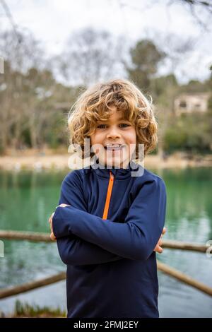 Happy child in blue clothes with folded arms looking at camera against water in daylight Stock Photo