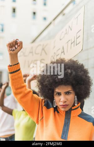 Young African American Woman with afro hair standing with fist up protesting during Black Lives Matter demonstration in city Stock Photo