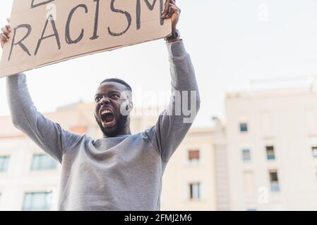 Low angle of African American male activist with poster screaming on city street during Black Lives Matter protest Stock Photo