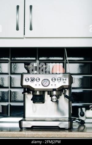 Professional stainless steel coffee machine with manometer and ceramic cup on table against glass block wall in house Stock Photo