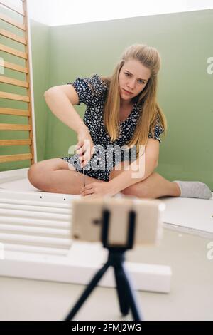 Young expectant female using screwdriver while assembling baby cot and sitting on floor at home Stock Photo