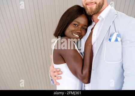 Cheerful young multiethnic couple wearing elegant stylish clothes hugging on street and looking at camera Stock Photo