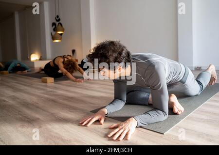 Flexible male practicing yoga in Kapotasana while stretching legs during yoga class in studio Stock Photo