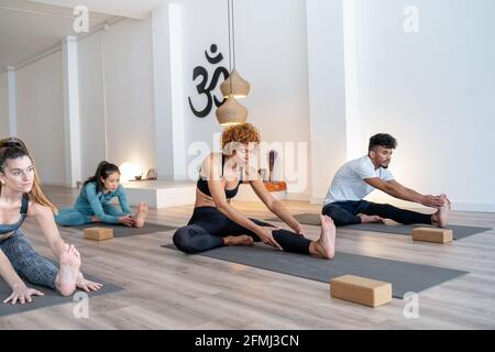 Company of multiethnic focused people in activewear sitting on mats in forward bend pose and practicing yoga together in studio Stock Photo
