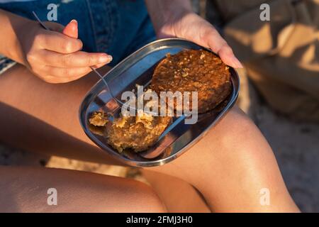From above of crop unrecognizable female traveler sitting on rock and eating tasty food during hiking in summer Stock Photo