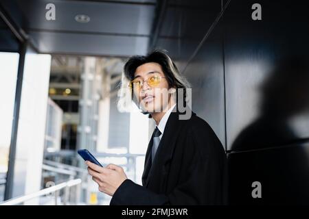 Young attentive Asian male executive in formal apparel and sunglasses text messaging o looking away Stock Photo