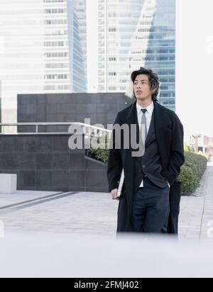 Young ethnic male executive in coat with hand in pocket and netbook looking away while strolling in city Stock Photo