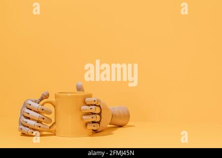 Creative ornamental wooden hand holding colorful mug on yellow background in studio Stock Photo