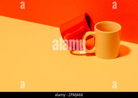 Creative colorful mugs on yellow and red background in studio Stock Photo