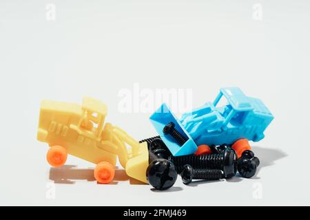 From above of small plastic toy tractor collecting various black screws on white table Stock Photo