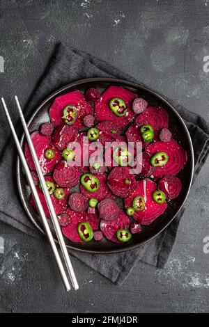 Top view composition of tasty beetroot slices arranged on baking pan with green jalapeno peppers and placed on black towel on kitchen table close to c Stock Photo