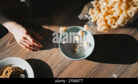 Crop unrecognizable person pouring milk into bowl with delicious corn rings for breakfast on wooden table Stock Photo