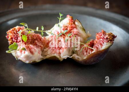 Closeup of tasty ripe fig slices with aromatic thyme sprigs on plate on wooden surface Stock Photo
