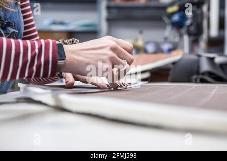 Crop unrecognizable female sewer making piece of cloth while working in workshop and creating upholstery for motorcycle seats Stock Photo