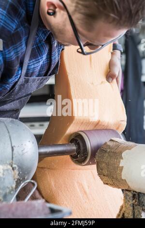 Male artisan polishing piece of foam rubber with electric grinder while making seat for motorcycle in workshop Stock Photo